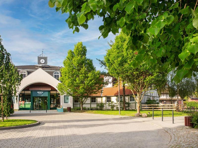 Hotelentree met paviljoen omgeven door bomen en een geplaveerde parkeerplaats