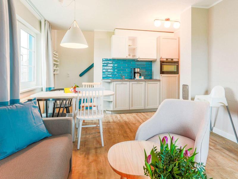 Lichte woonkamer met blauw kussen, eetgedeelte en moderne keuken met turquoise tegels.