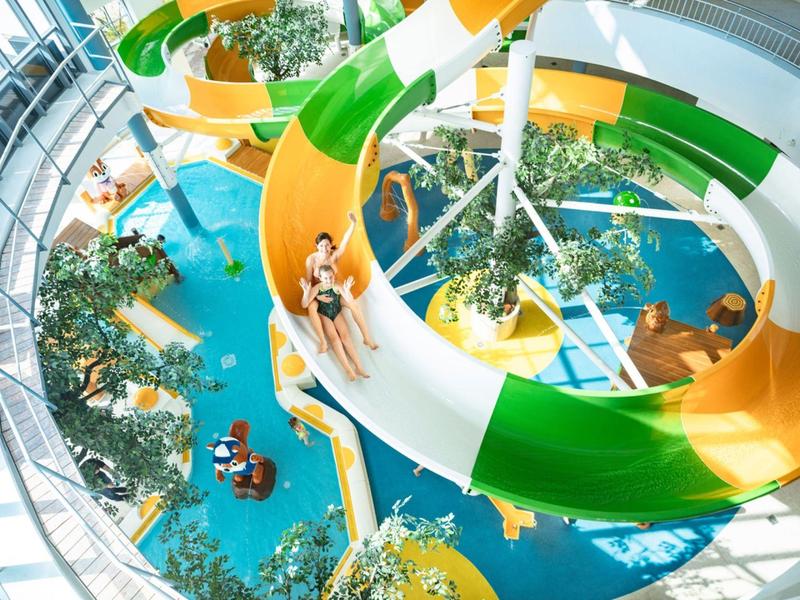 Mensen glijden van kleurrijke waterglijbanen in een overdekt waterpark met planten.