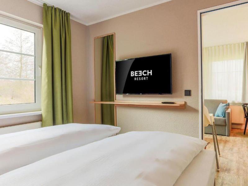 Modern hotelkamer met twee bedden, groot raam en aan de muur gemonteerde tv.