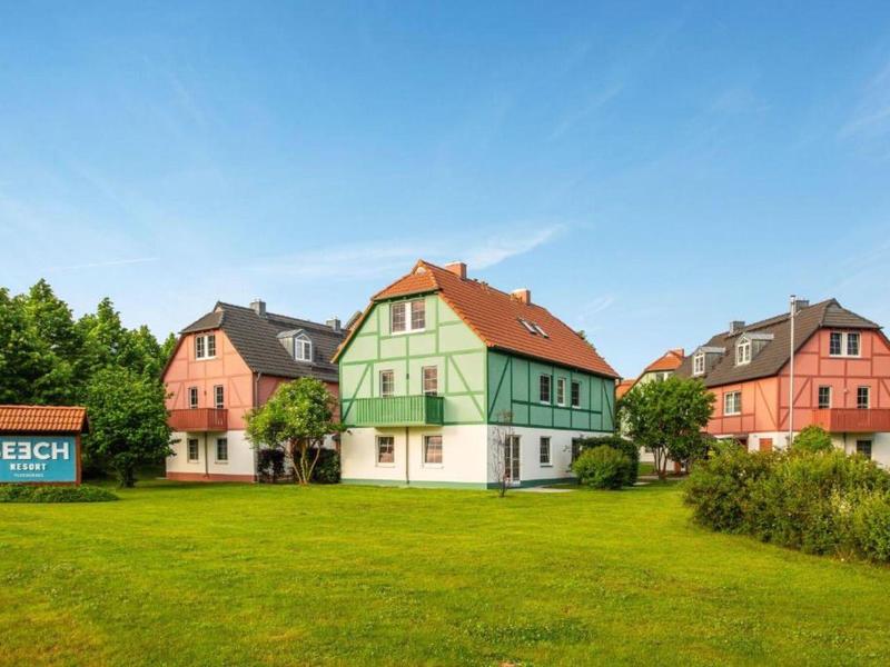 Meerdere vakantiehuisjes met grasveld onder een blauwe hemel en een bord met 'Beach'.