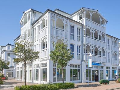Großes weißes Hotelgebäude mit Holzbalkonen und zwei Bäumen davor.