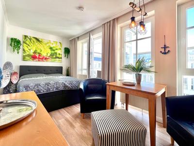 Chambre d'hôtel lumineuse avec lit, coin salon et grande fenêtre avec rideaux.