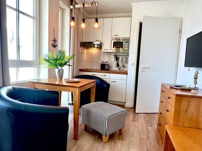 Coin cuisine chaleureux avec commode en bois, fauteuil bleu et petit ottoman.