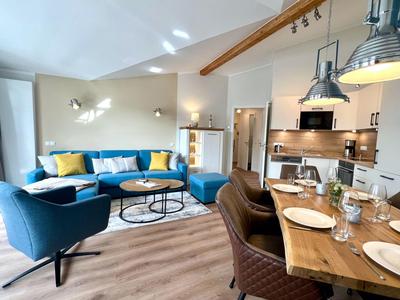 Espace de vie moderne avec fauteuils bleus, canapé, table en bois et cuisine ouverte dans un espace lumineux.