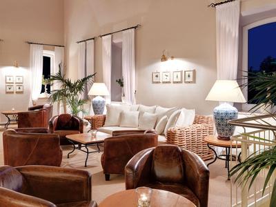 Przytulny pokój hotelowy z wygodnymi fotelami, sofami i ciepłym światłem lamp.