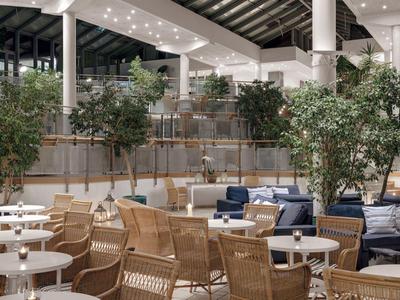 Modernes Hotelrestaurant mit vielen Holztischen, Stühlen und grünen Pflanzen.