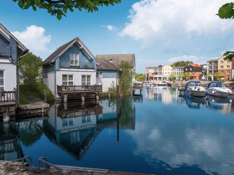 Picturesque houses on calm water of a marina with clear reflection and blue sky.