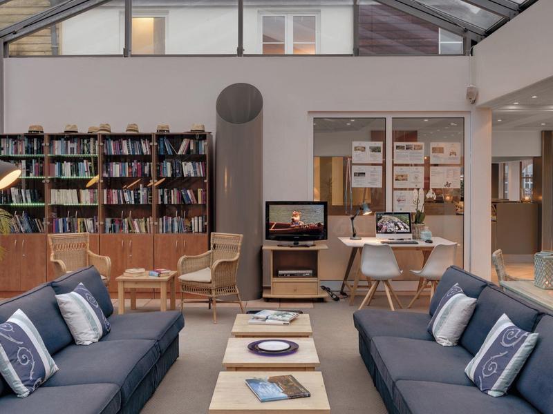 Modern living room with two blue sofas, coffee table, bookshelf, and large sunroom