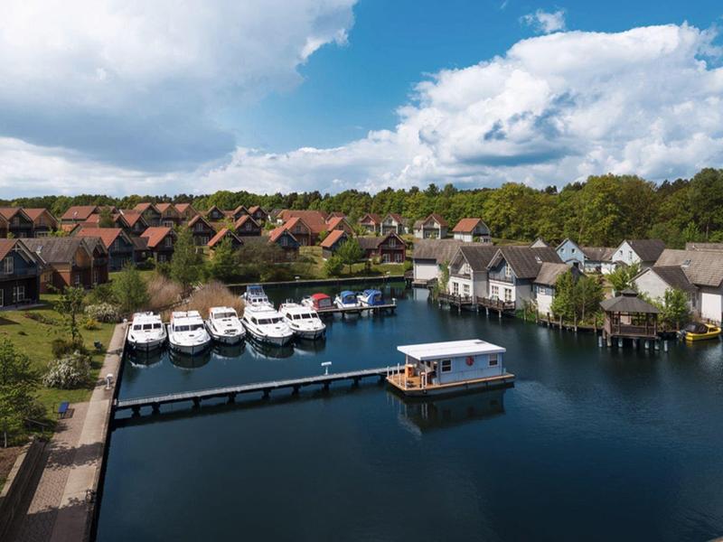 View of a holiday resort with a boat dock and several boats on a lake under cloudy sky.