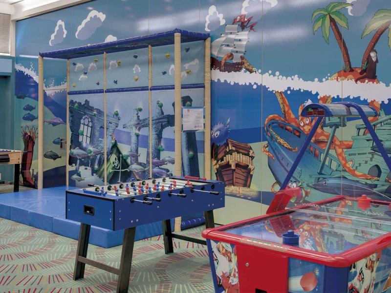 Colorful game room with air hockey, foosball, and pinball against a tropical mural wall.