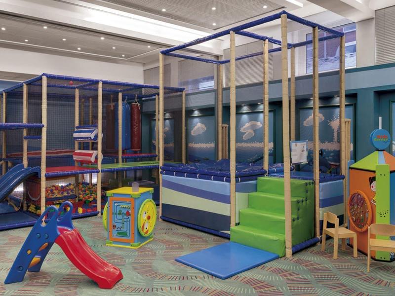 Colorful indoor playground with slide, climbing frame, and small tables in a hotel area.