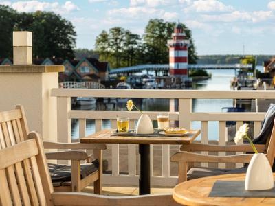 Terrasse mit Holztischen und Blick auf Hafen mit Leuchtturm und Booten