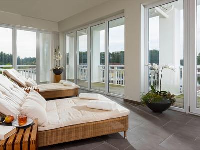 Heller Wellnessraum mit bequemen Liegen und Blick auf einen Balkon mit weißen Geländern.