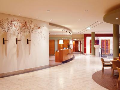 Jasna lobby hotelowa z dużą recepcją, kremową podłogą i kwiatowymi dekoracjami na ścianach.