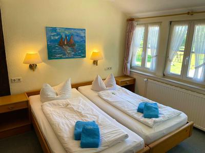 Twee eenpersoonsbedden met wit beddengoed en blauwe handdoeken in een lichte hotelkamer.