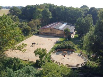 Paardensportlocatie met zandbak en meerdere paddocks, omgeven door bomen en velden.