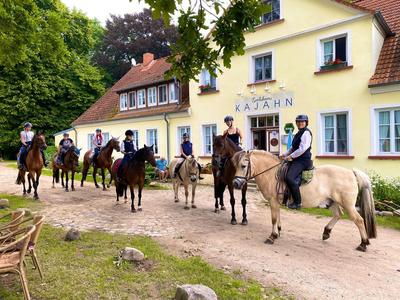 Groep ruiters op paarden voor een geel herberg in een landelijke omgeving