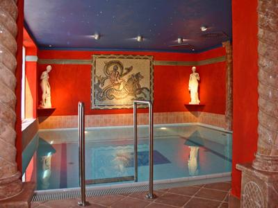 Indoor pool in a room with red walls, two statues, and a large artwork on the wall.