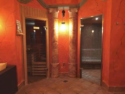 Cozy spa area with sauna and steam room, orange walls and two marble columns in the center.