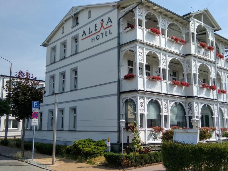 White multi-story hotel building with balcony flowers and clear windows under a cloudy sky.