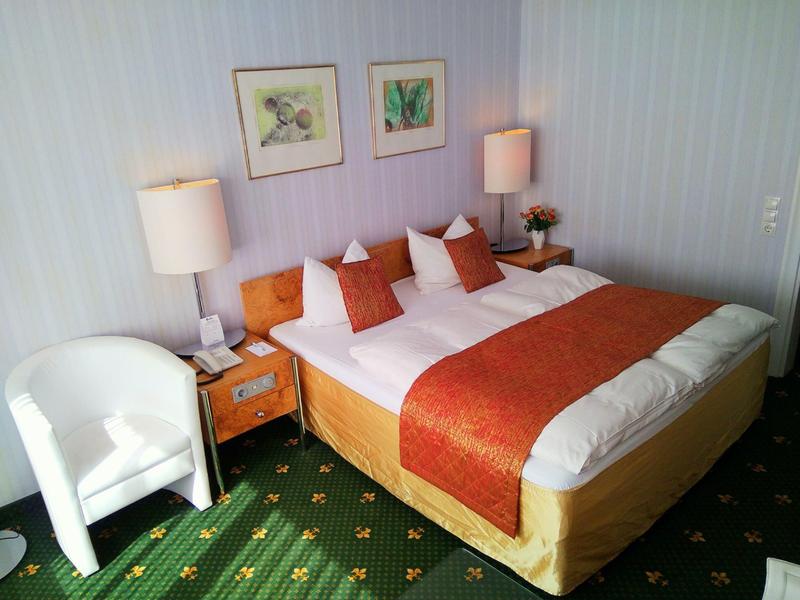 Cozy hotel room with double bed, white walls, and green carpet flooring.