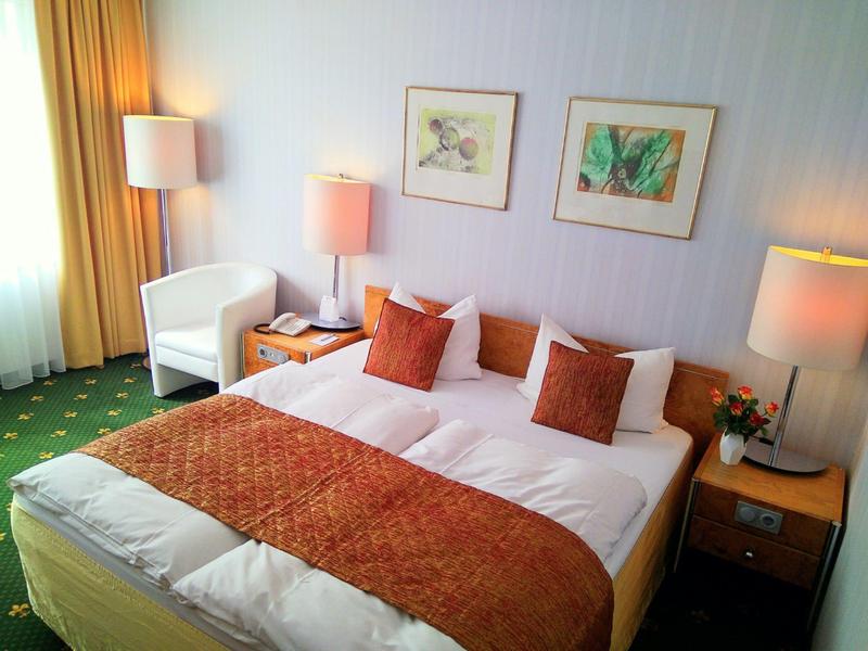 Modern hotel room with double bed, two nightstands, chair, and three lamps.