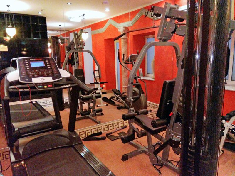 Gym room with various exercise machines and large mirrors on the walls.