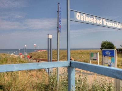 Pohled na přístup k pláži se znakem 'Ostseebad Trassenheide' a trávními dunami v popředí.