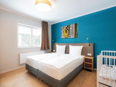 Helles Hotelzimmer mit Doppelbett, Babybett und blauer Akzentwand.