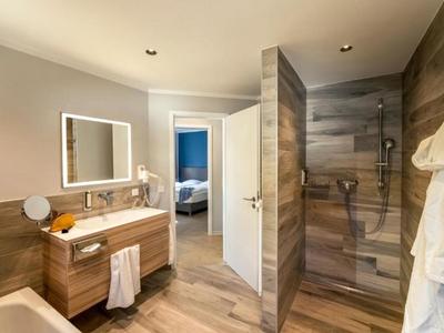 Helles Badezimmer mit Waschtisch, großem Spiegel und offener Dusche mit Holzakzenten.