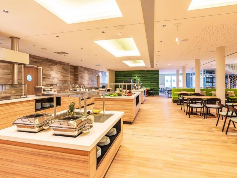 Světlá, moderní hotelová jídelna s dřevěným nábytkem a velkou bufetovou sekcí.