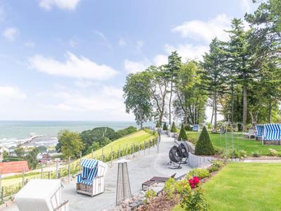 Un jardin bien entretenu avec des sentiers, des chaises de plage et une vue sur la mer sous un ciel bleu.