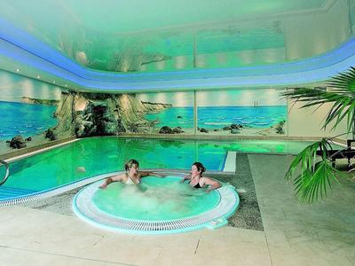 Piscine intérieure avec deux personnes dans un jacuzzi rond, entouré de fresques murales représentant des scènes de plage.
