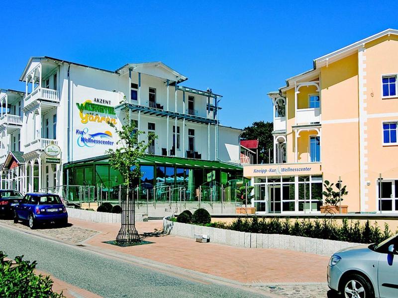 Straße mit zwei Hotels in hellen Farben und geparkten Autos bei klarem blauem Himmel.