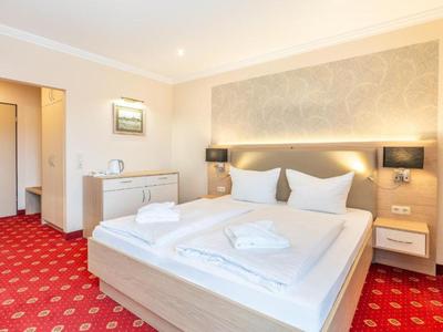 Modern hotel room with double bed, red carpet, and minimalist decor.