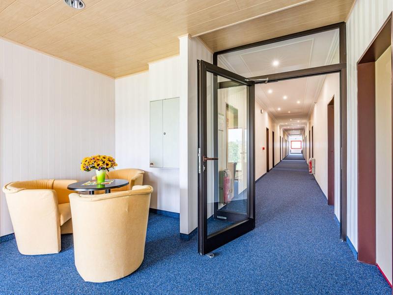 Hotel corridor with blue carpet, glass door, and seating area with table and chairs.