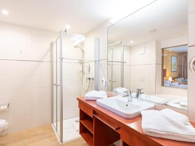 Helles Badezimmer mit Waschbecken, Spiegel und Dusche mit Glaswand.