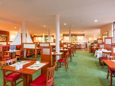 Helles Restaurant mit roten Stühlen, grünen Teppich und dekorativen Segelbooten auf Tischen