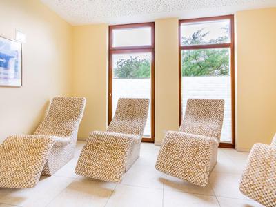 Heller Entspannungsraum mit vier gemusterten Liegestühlen vor großen Fenstern.