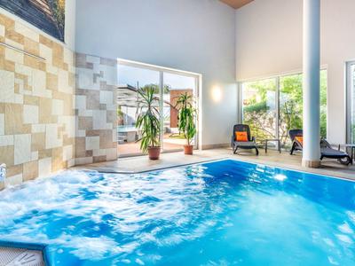 Innenpool mit blauer Beleuchtung, Pflanzen und großen Fenstern in einem modernen Spa-Bereich.