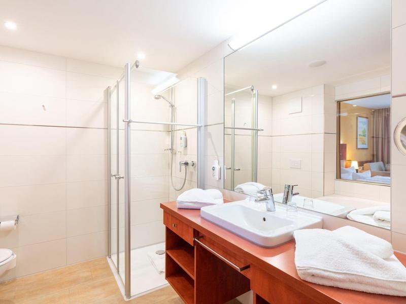 Helles Hotelbadezimmer mit einer Glasdusche, großem Spiegel und Waschtisch mit Handtüchern.