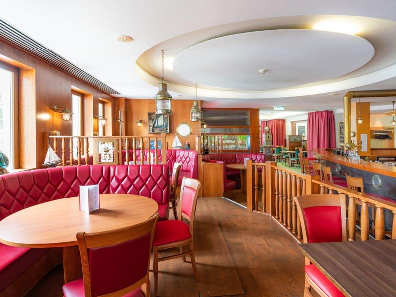 Gemütliche Hotelbar mit roten Sitzbänken, Holztischen und dekorativer Beleuchtung.