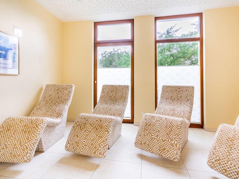 Heller Entspannungsraum mit vier gemusterten Liegestühlen vor großen Fenstern.