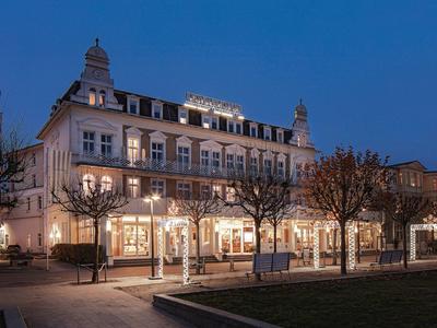 Beleuchtetes historisches Hotelgebäude bei Dämmerung mit Bäumen und Sitzbereichen davor.