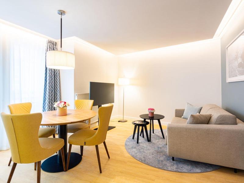 Bright living and dining area with yellow chairs, wooden floor, and modern sofa.