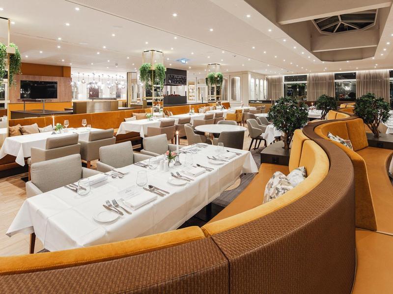 Modern restaurant interior with white tablecloths and seating in warm colors.
