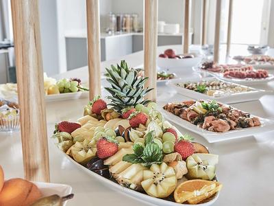 Bufet z różnymi owocami i daniami śródziemnomorskimi na stołach w jasnym pomieszczeniu.