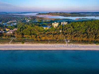 Vista aerea di una spiaggia con acqua turchese, ombrelloni e foreste sullo sfondo.