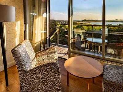 Accogliente zona soggiorno con poltrone e tavolo davanti a finestre a tutta altezza che si aprono su una terrazza con vista.